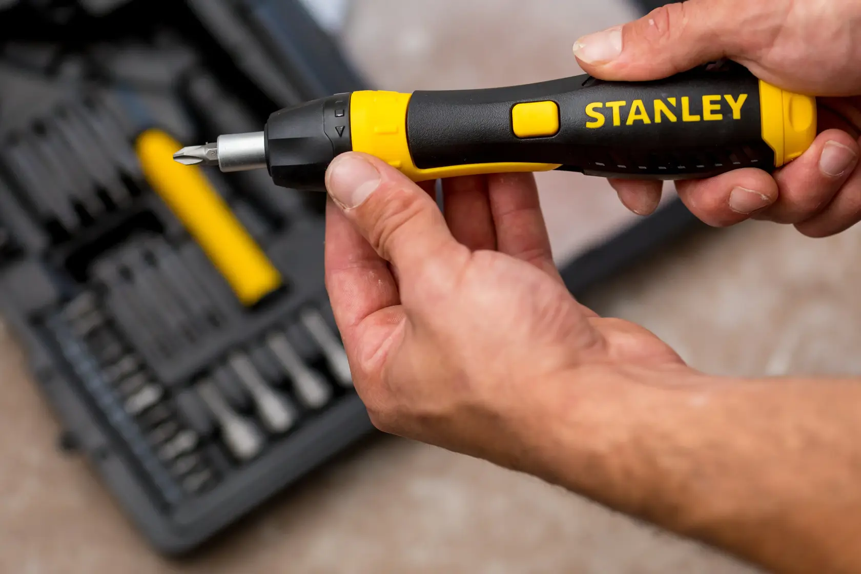 STANLEY 0-63-038 ratcheting screwdriver with black and yellow handle held in hand, tool kit in background.