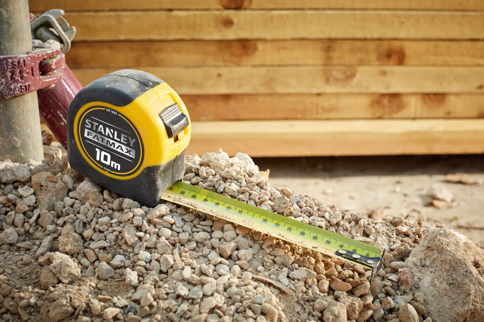Stanley 33-829 tape measure with yellow casing on rocky ground, tape extended, wooden boards in background.