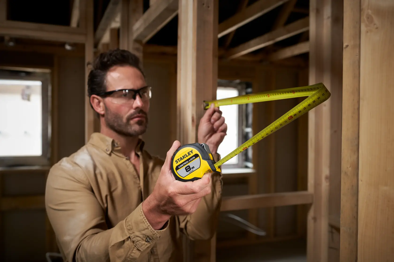 Photo of STANLEY STHT37232 tape measure in use at a construction site, measuring wooden framing.