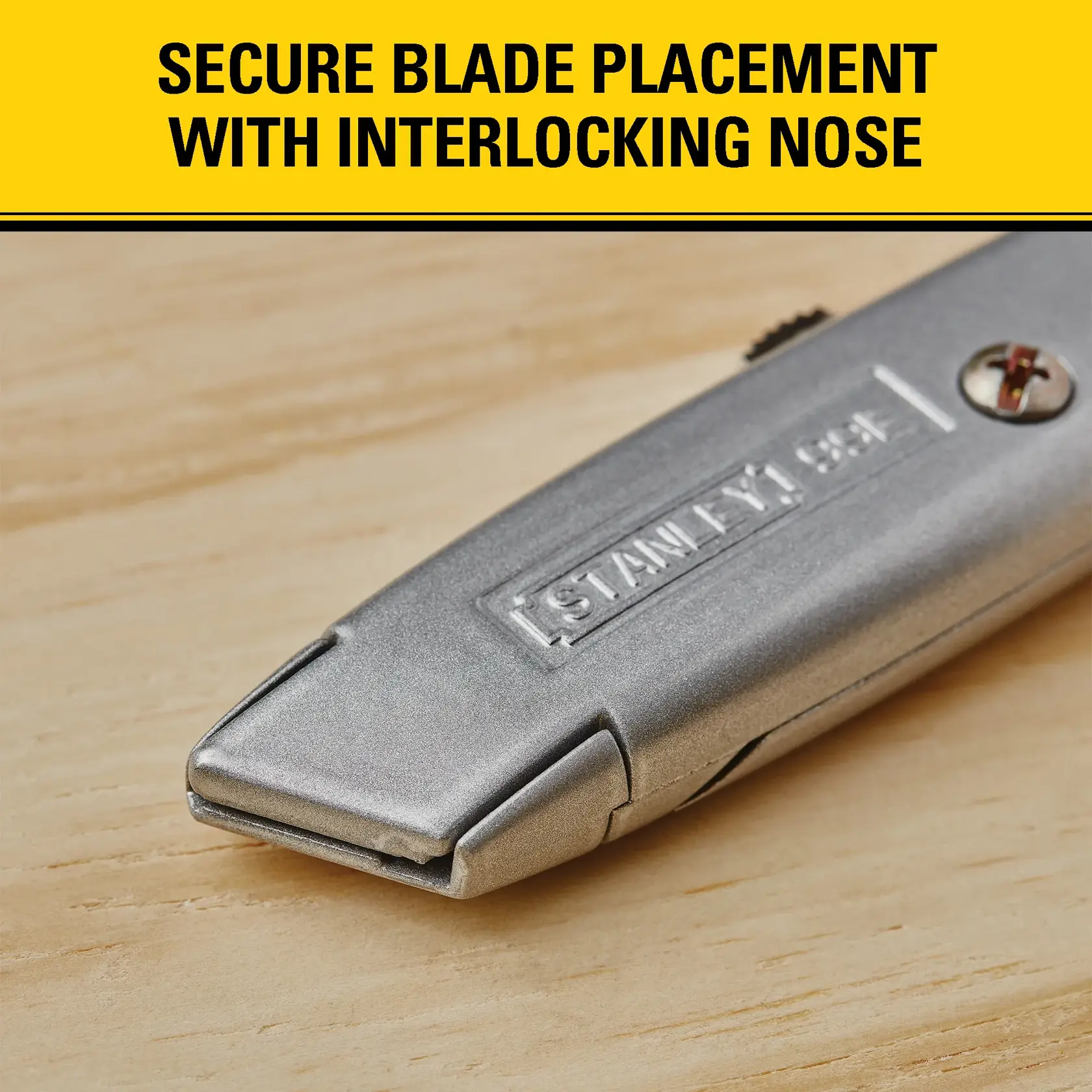 Close-up of a STANLEY 10-099 utility knife showing the interlocking nose feature for secure blade placement on a wooden surface. The image includes a yellow banner with the text: 'SECURE BLADE PLACEMENT WITH INTERLOCKING NOSE.'
