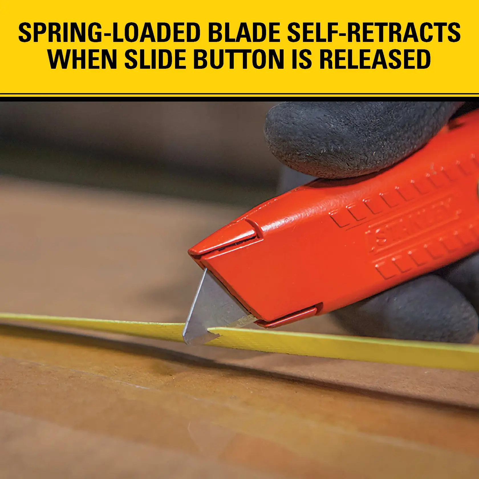 A close-up of a hand wearing a glove using a red STANLEY utility knife to cut yellow tape on a cardboard box. The image features text stating that the spring-loaded blade self-retracts when the slide button is released.