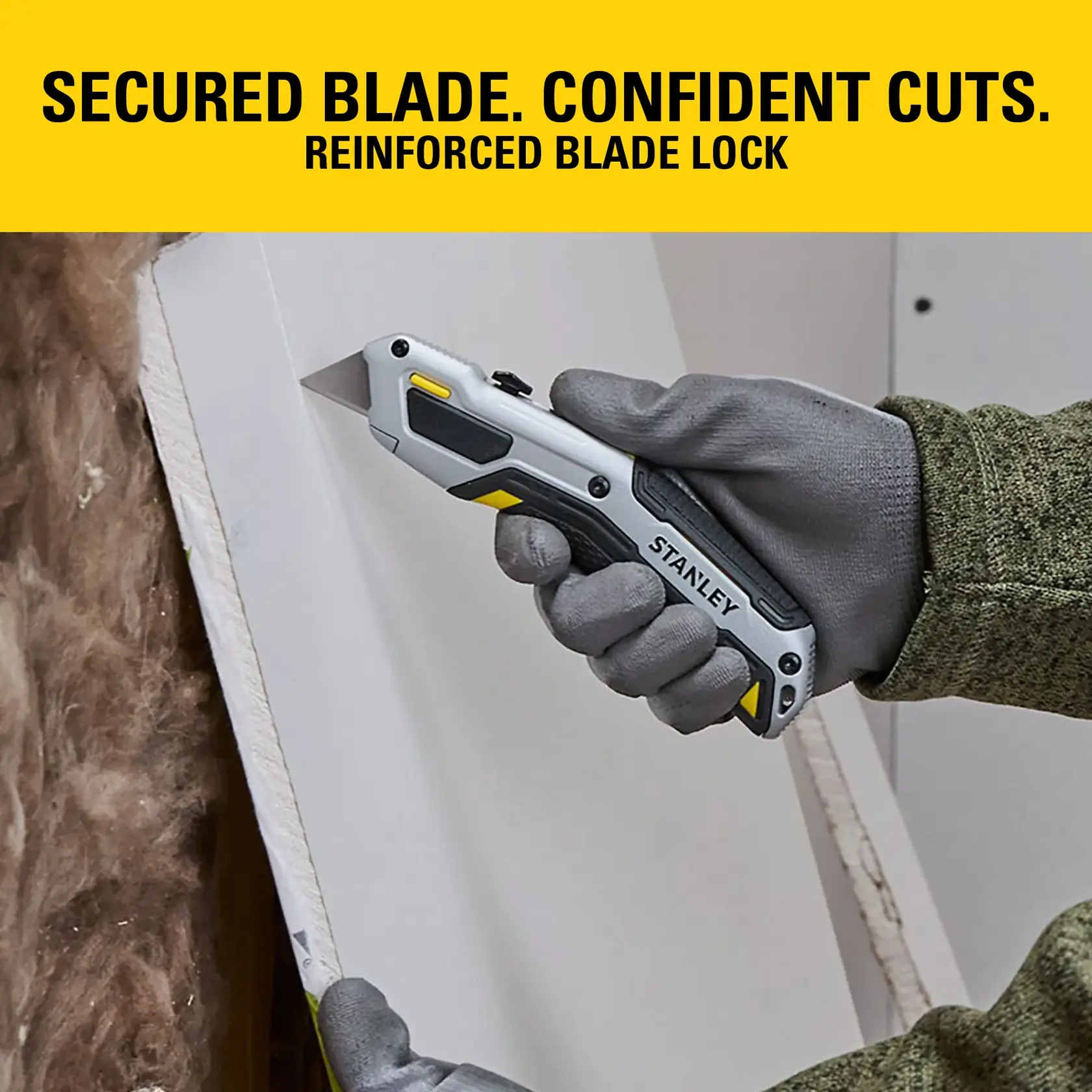 Stanley utility knife with reinforced blade lock, held by gloved hand cutting drywall.