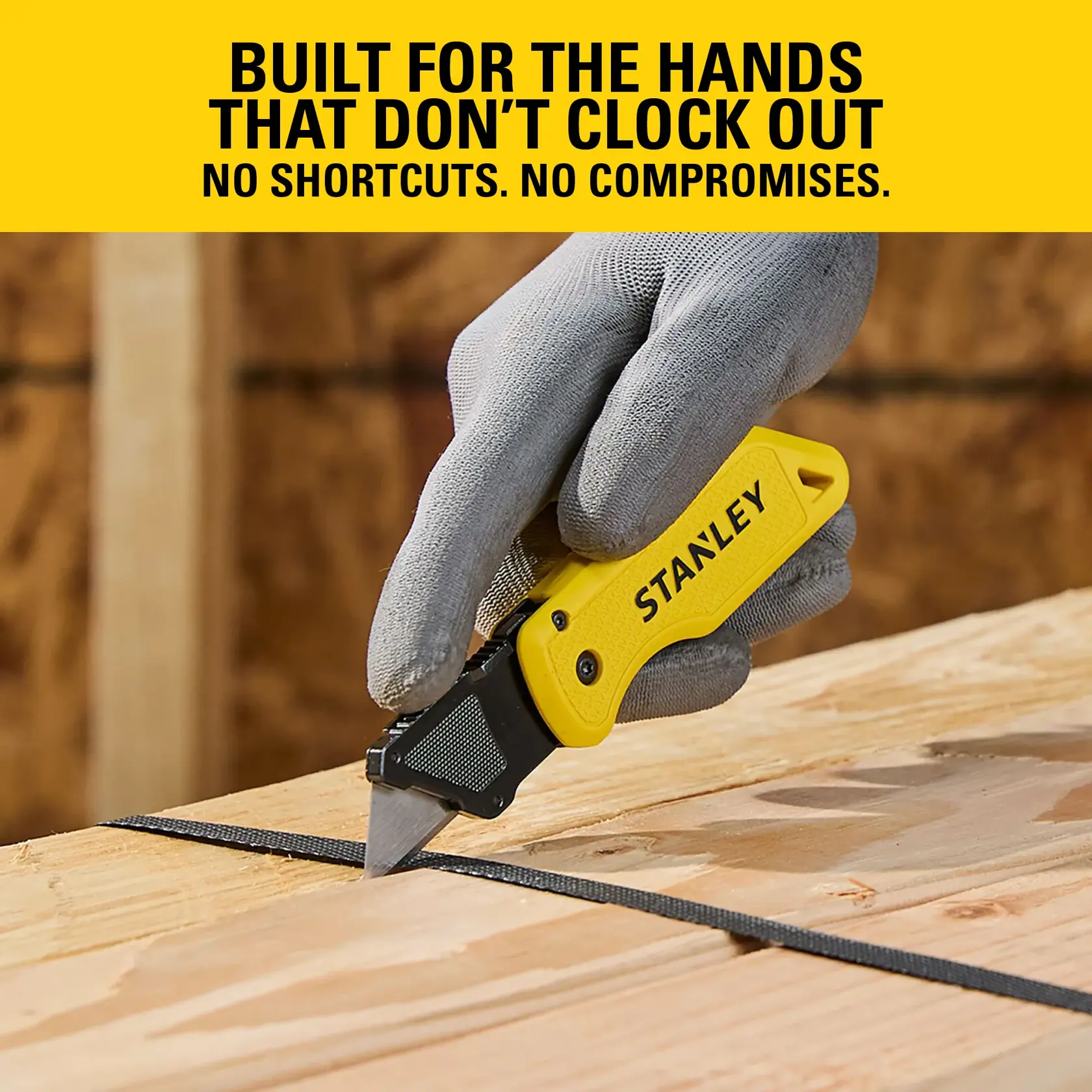 Gloved hand using a yellow STANLEY utility knife to cut black strap on wooden surface in a workshop.