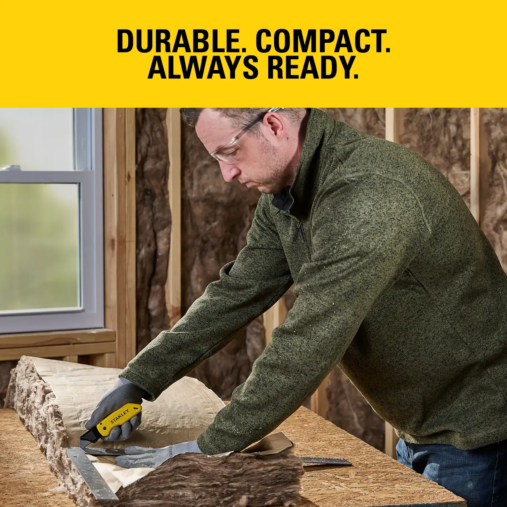 Person uses yellow Stanley utility knife to cut material on workbench in construction area.