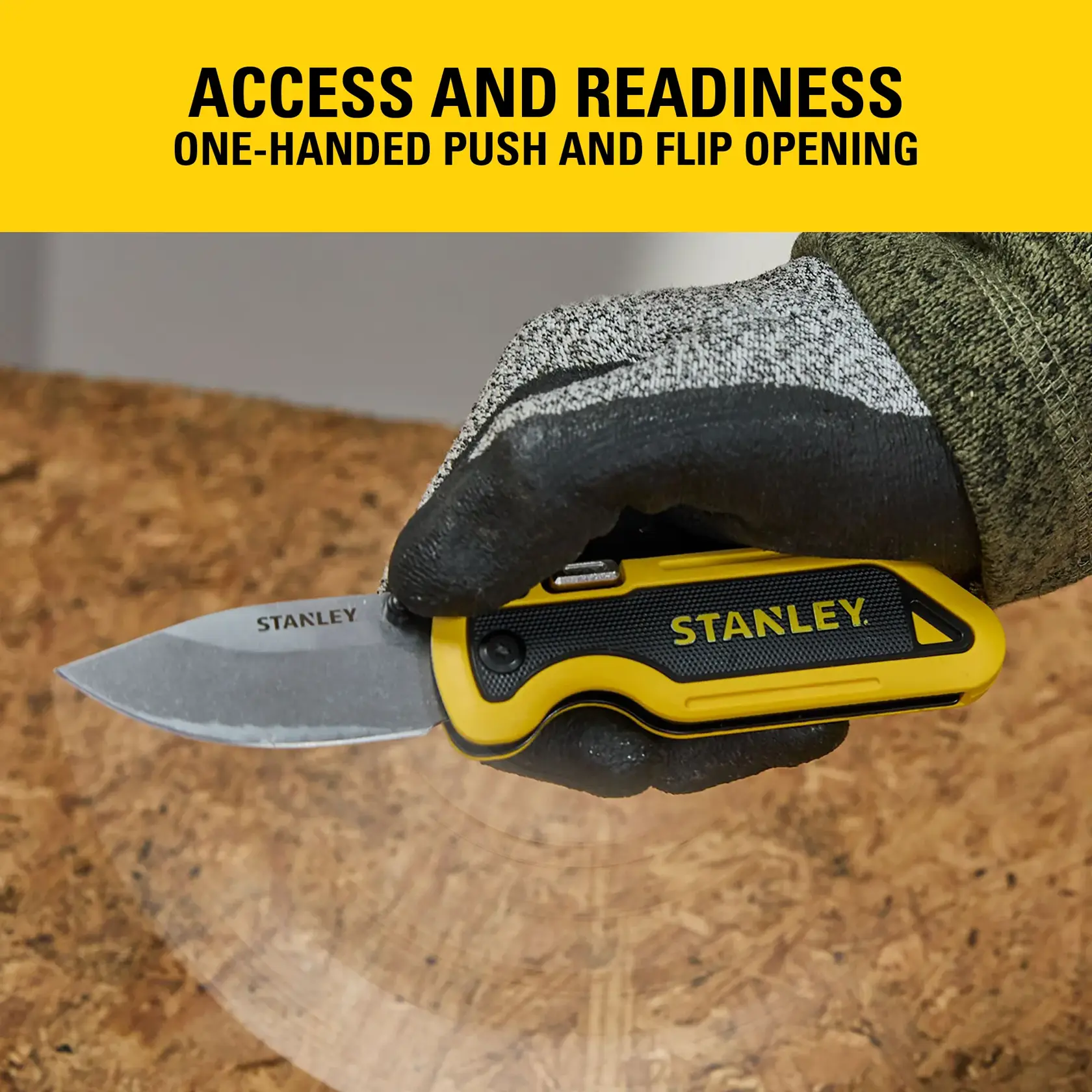 Stanley folding knife held in gloved hand, showing one-handed push and flip opening feature on a work surface.