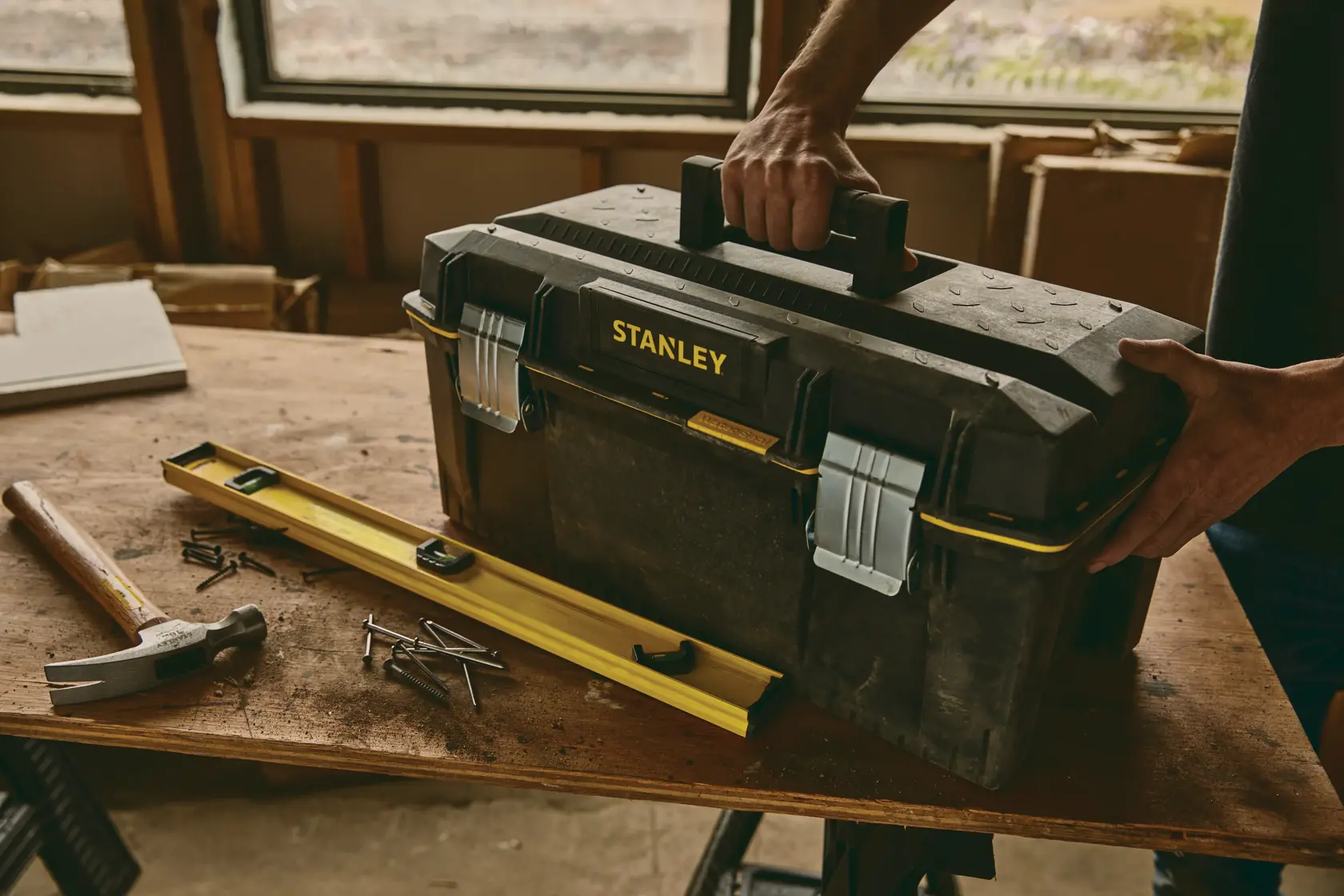 STANLEY 023001W toolbox on workbench with hammer, nails, and level, person holding handle, workshop background.