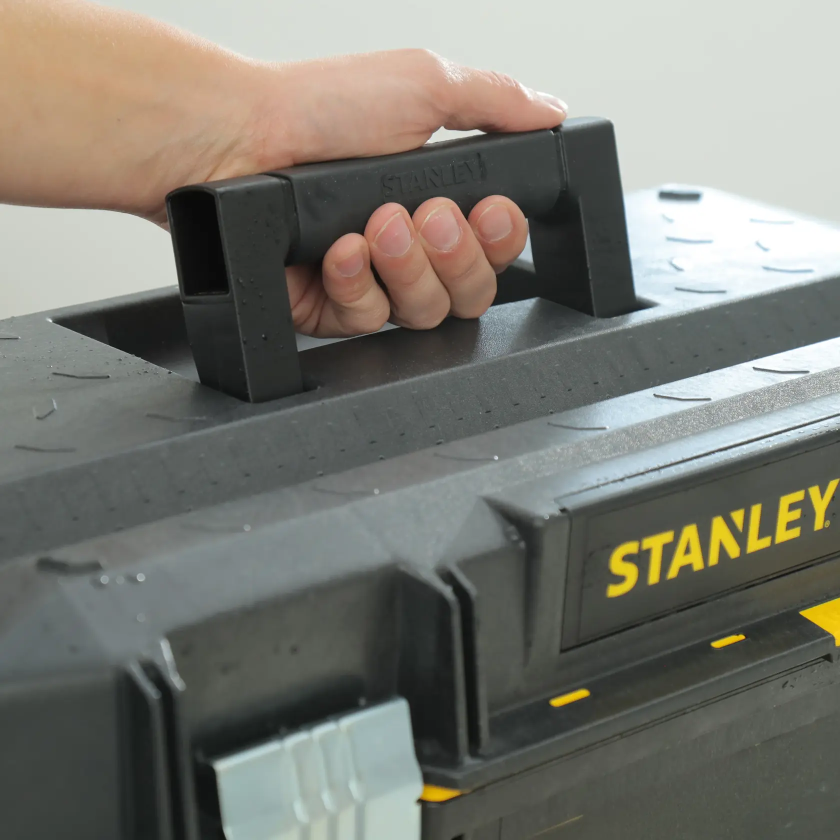 STANLEY 023001W FATMAX toolbox close-up, black handle held by hand, yellow label visible.