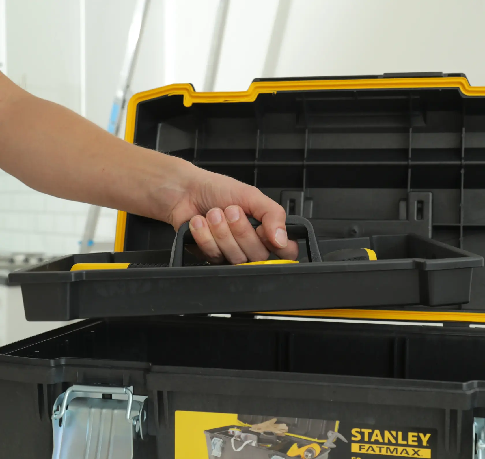 STANLEY 023001W toolbox close-up with a hand lifting the removable tray, black and yellow plastic construction.