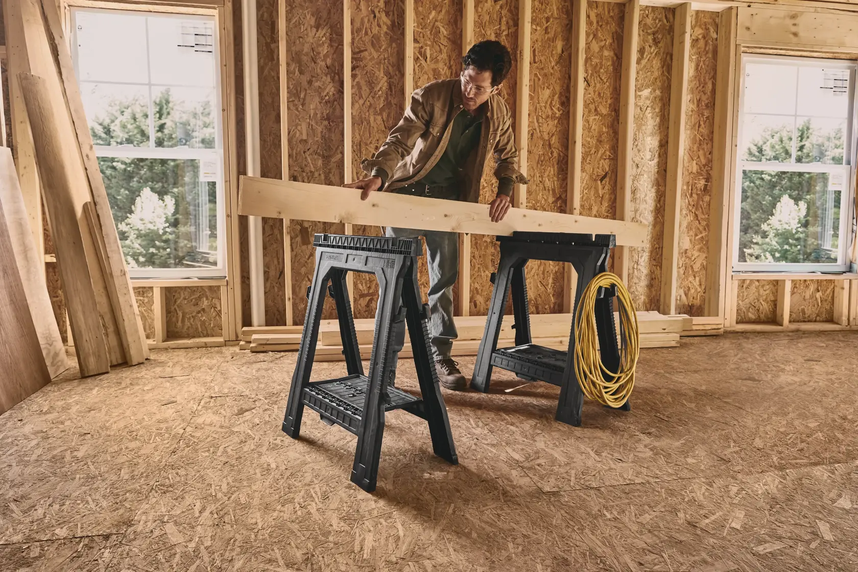 STANLEY 060864R plastic sawhorses in use at construction site, supporting wooden beam and yellow cord.