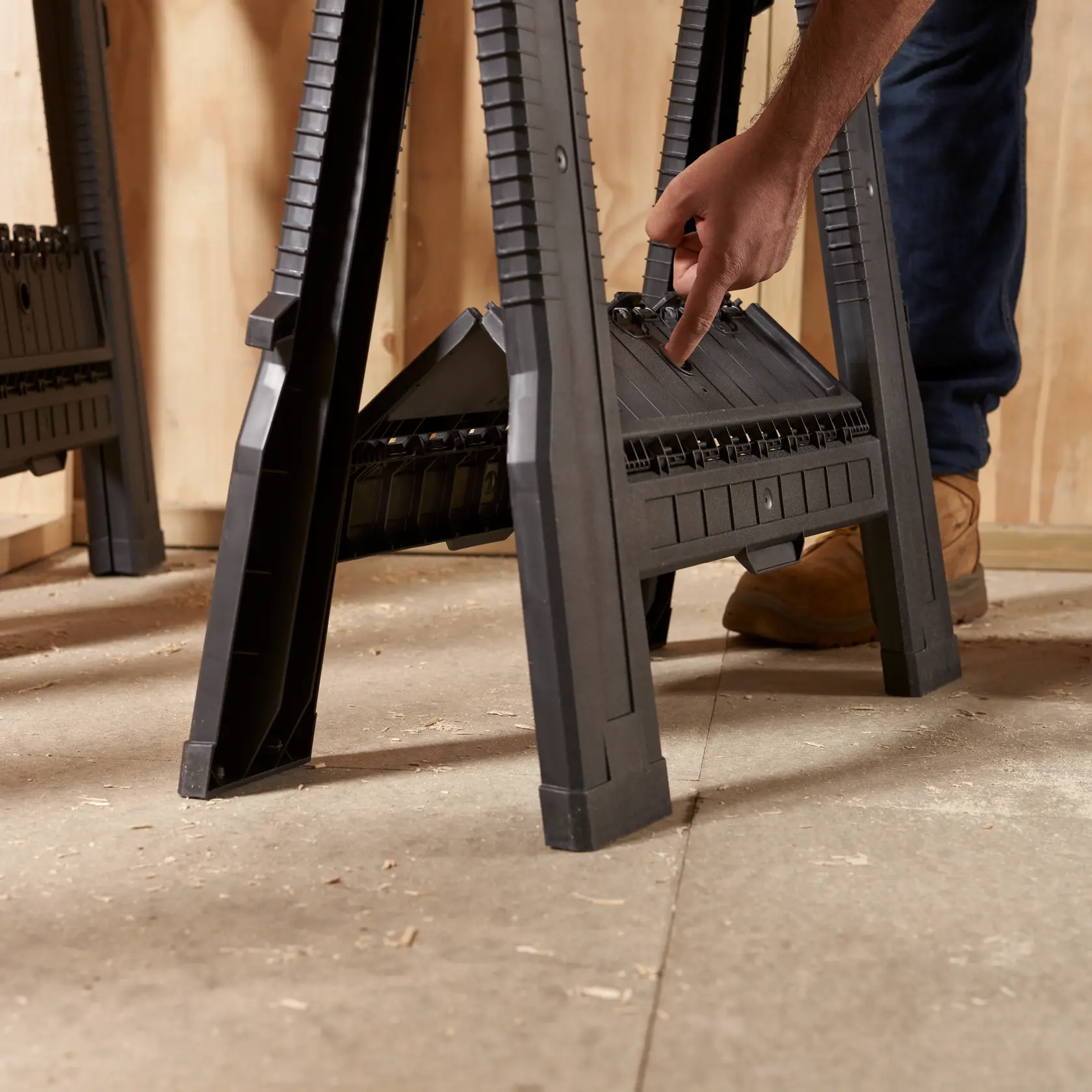 STANLEY 060864R black plastic sawhorse in workshop, close-up side angle with hand adjusting center shelf.