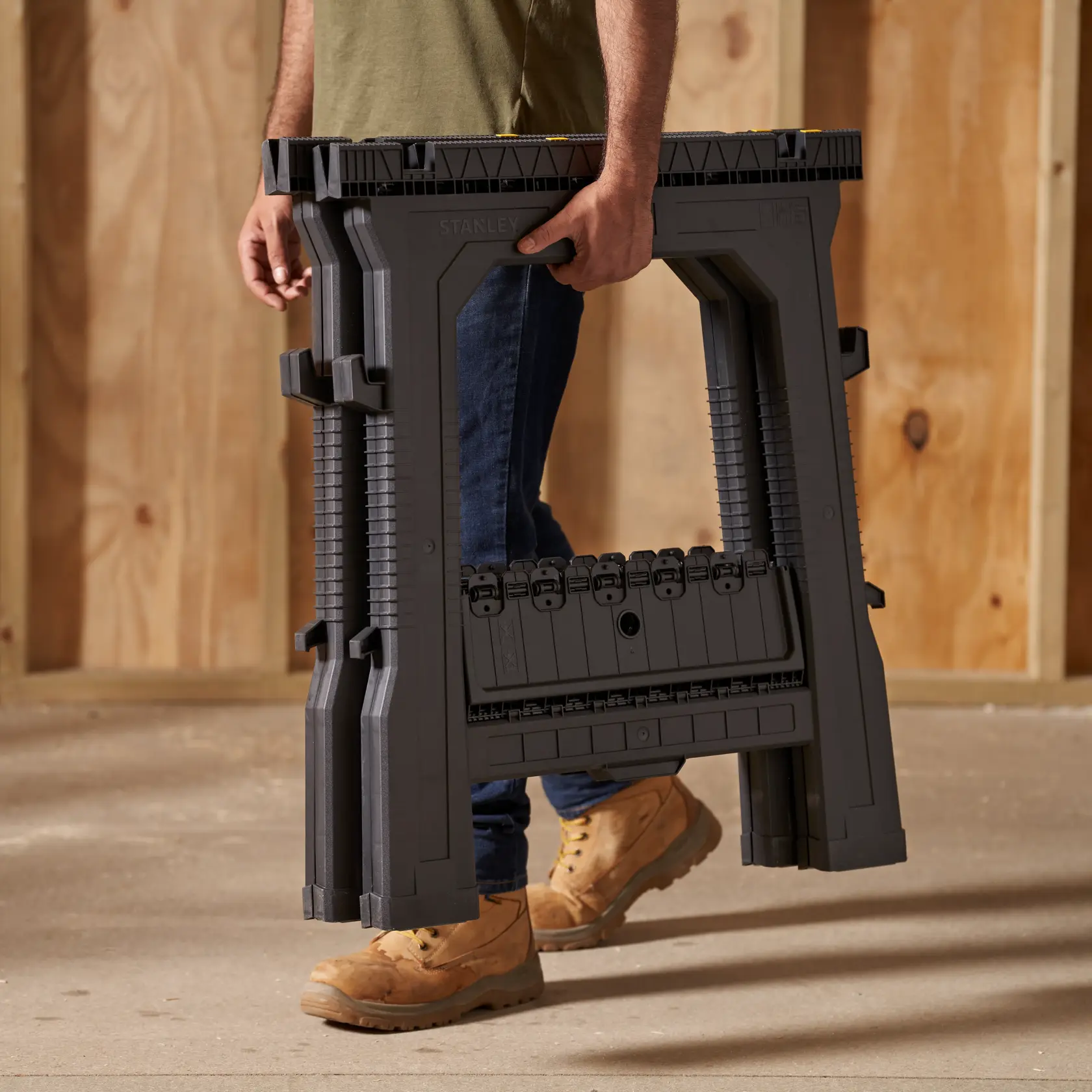 STANLEY 060864R folding saw horse, dark gray, shown being carried by a person, product photography.