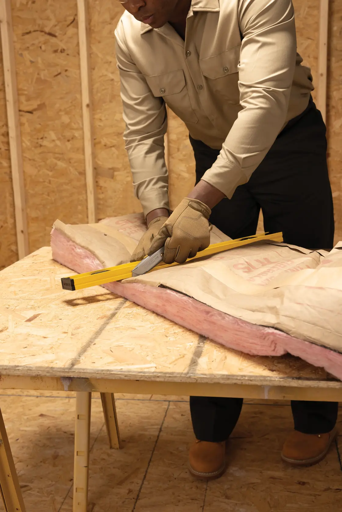 STANLEY 10-099 utility knife cutting insulation on workbench, worker wearing gloves in construction setting.