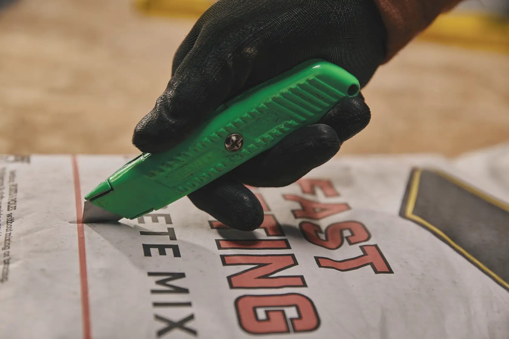Stanley 10-179 green utility knife cutting open concrete mix bag, close-up, held with black work glove.