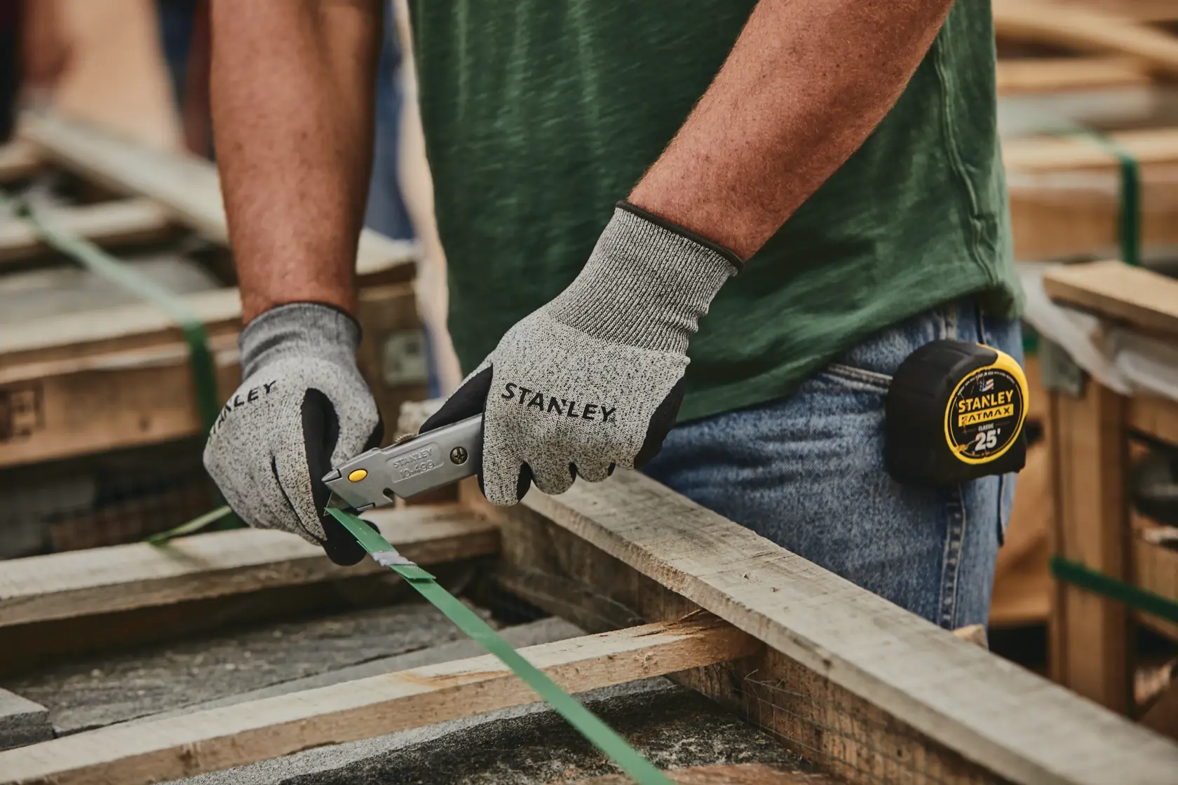 Stanley 10-499 utility knife in use, worker with gloves cutting green strapping on wooden pallet.