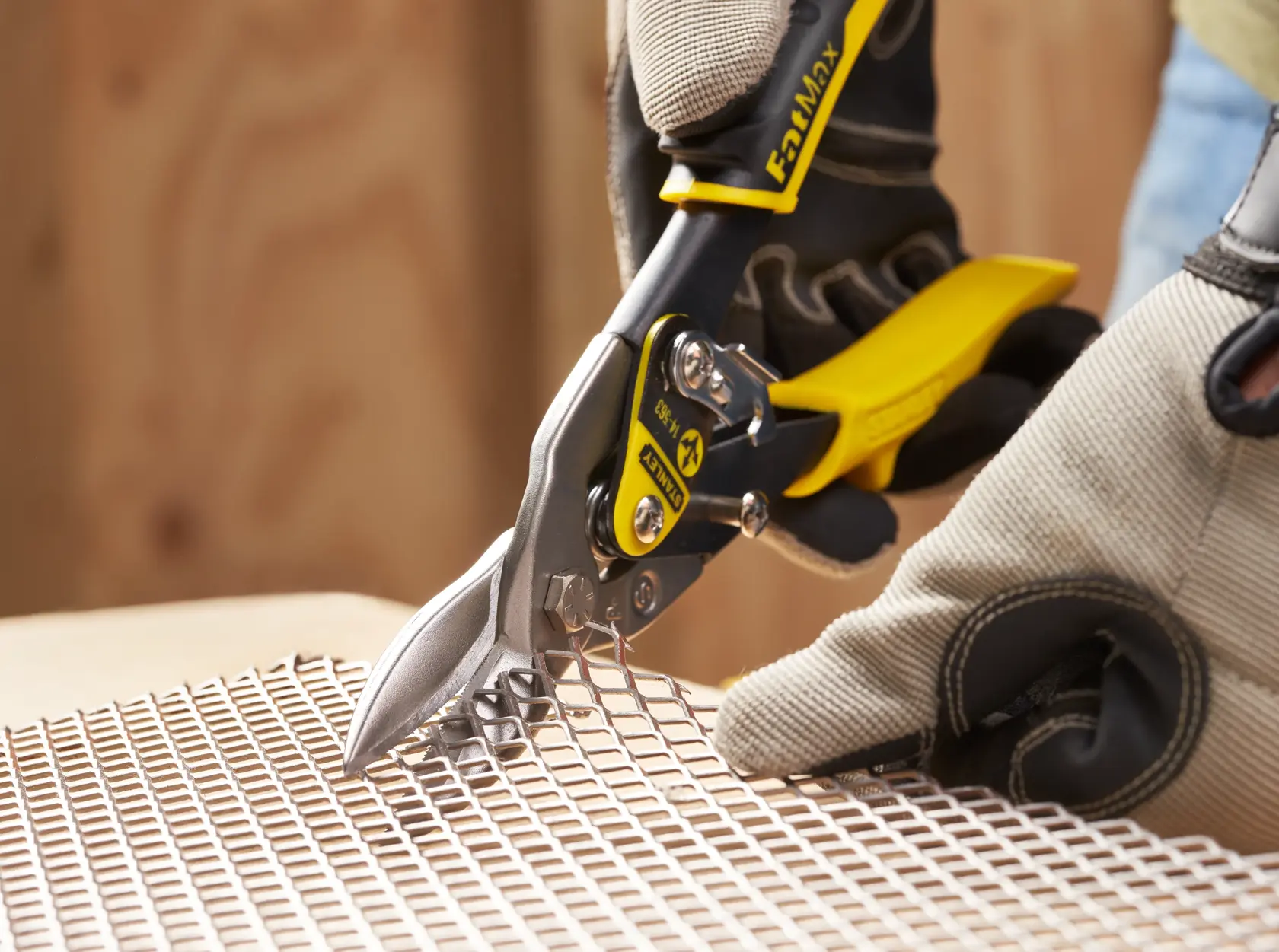 Photo of STANLEY 14-563 aviation snips cutting metal mesh, close-up, with gloved hands for safety.