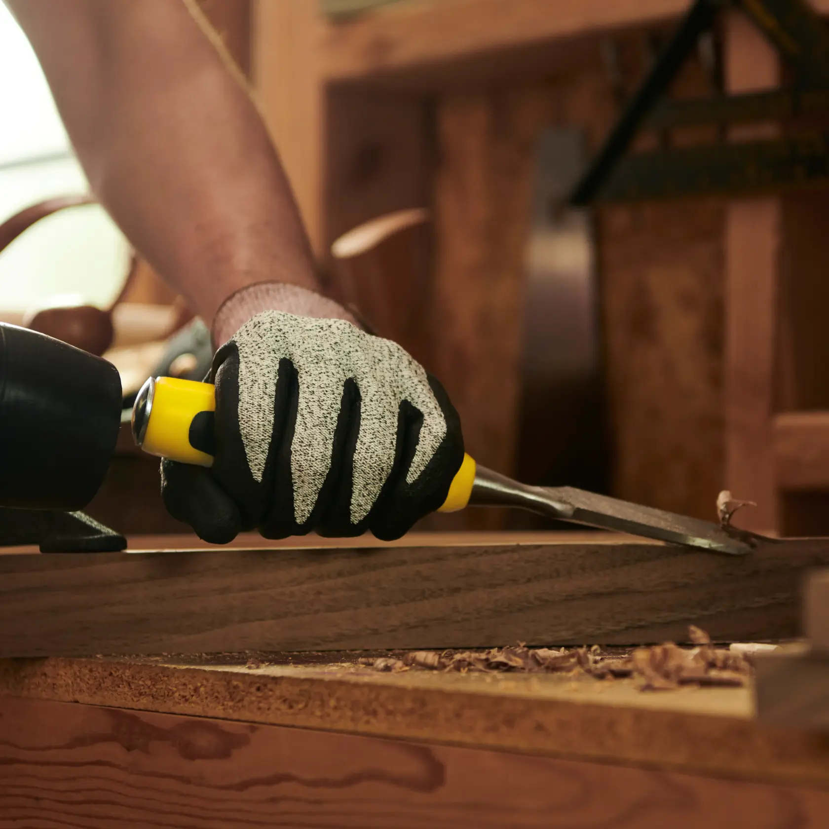STANLEY 16-316 chisel held by gloved hand carving wood on workshop table, close-up angle.