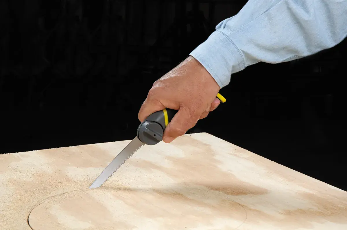 Photo of STANLEY 20-092 hand saw cutting a circular shape in plywood, held by a person in a light blue shirt.