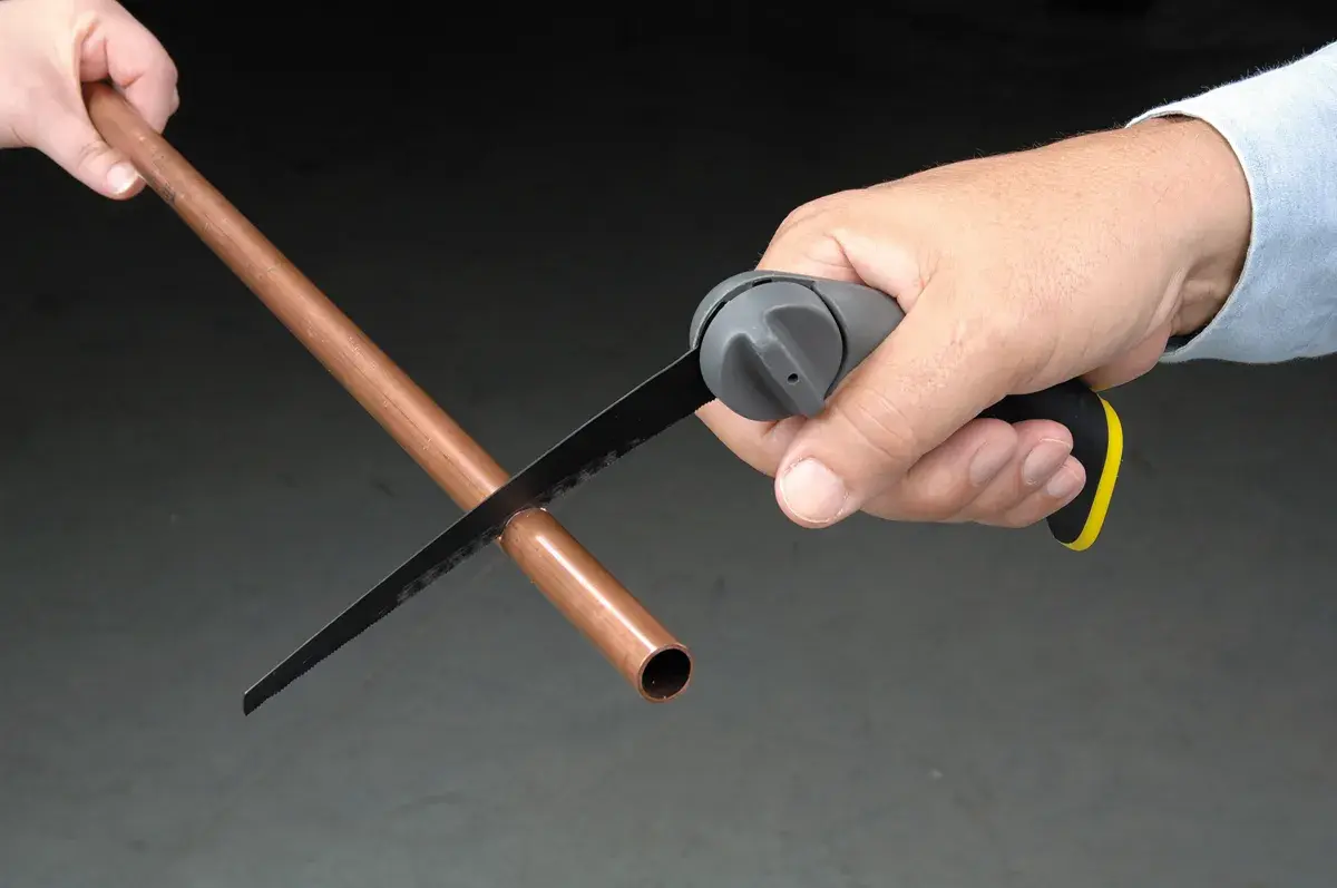 Photo of STANLEY 20-092 hand saw cutting a copper pipe, handheld, close-up view.