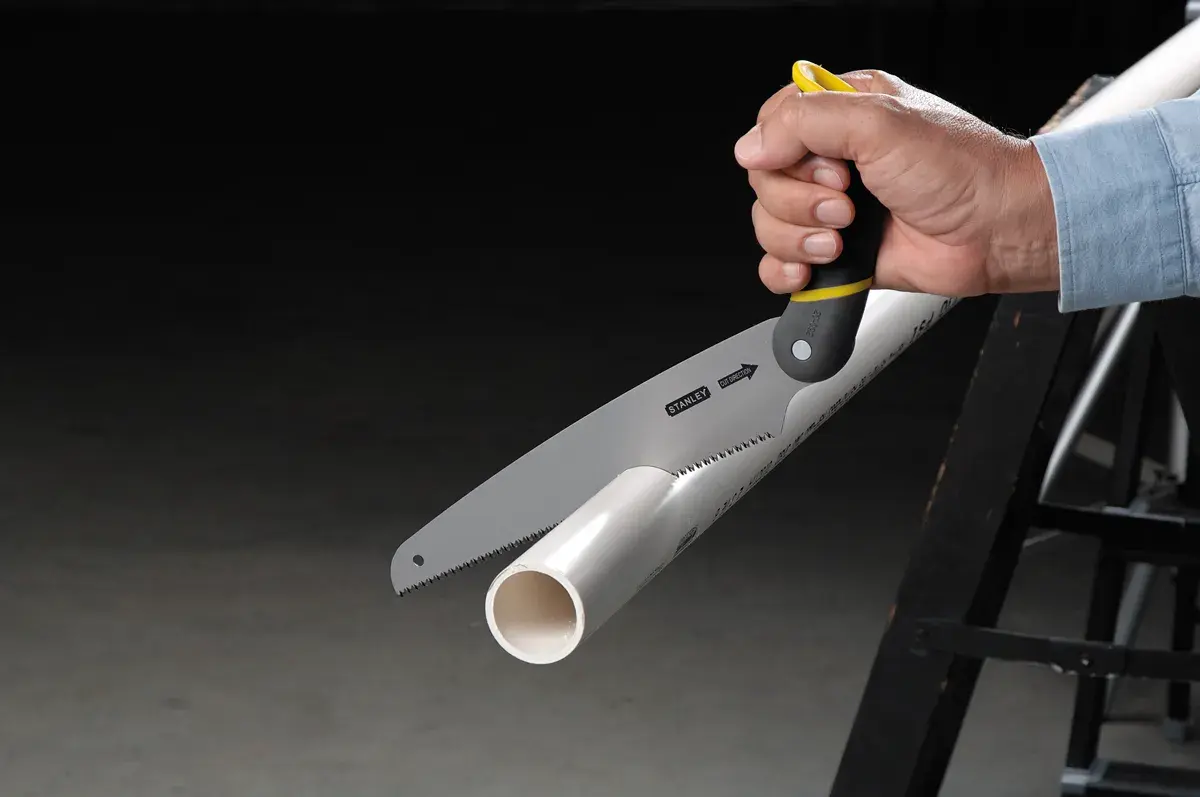 STANLEY 20-092 hand saw cutting white PVC pipe, close-up side view showing black and yellow handle.