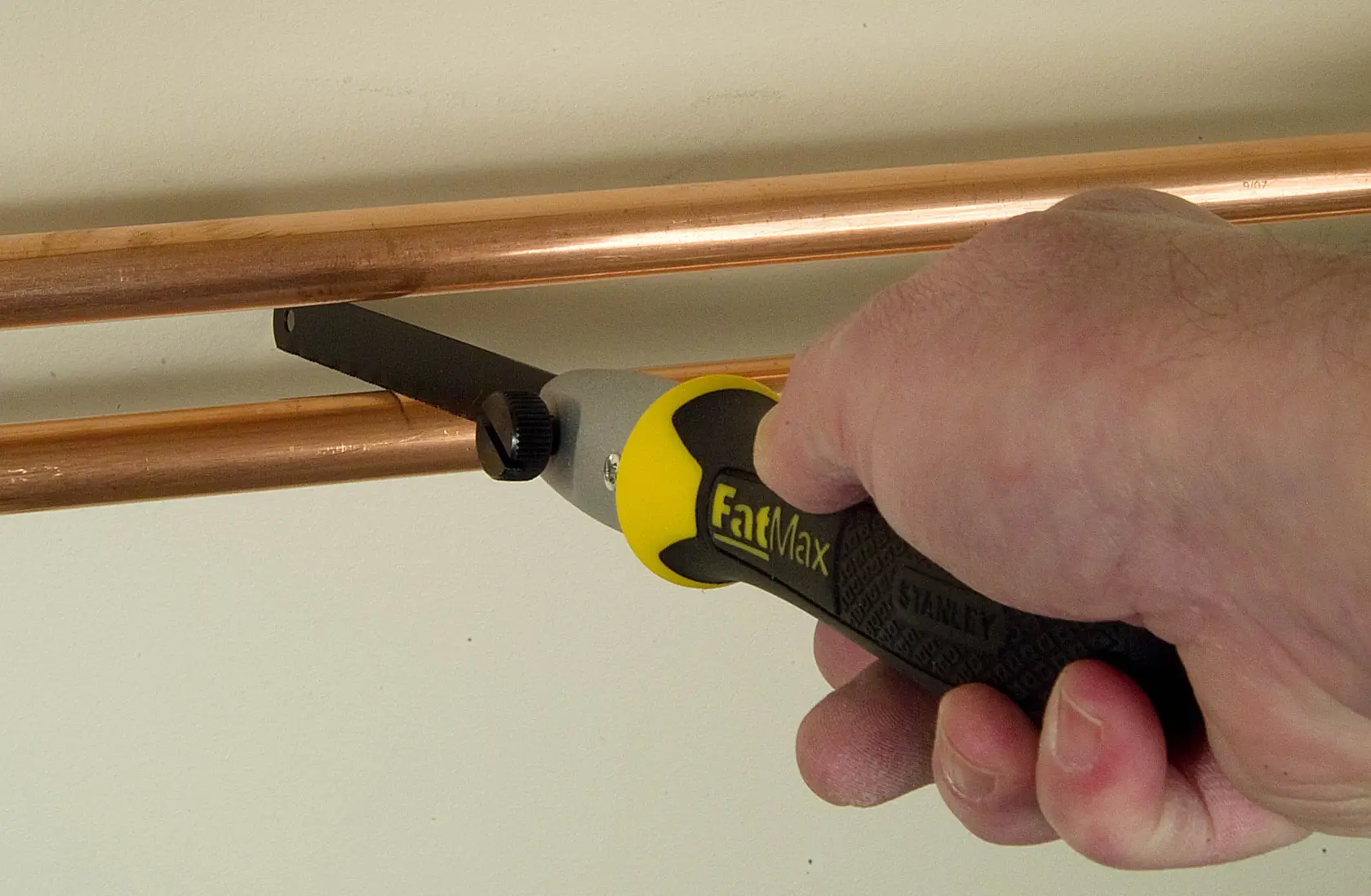 Stanley 20-220 FatMax hand saw cutting copper pipe, close-up, yellow and black handle.