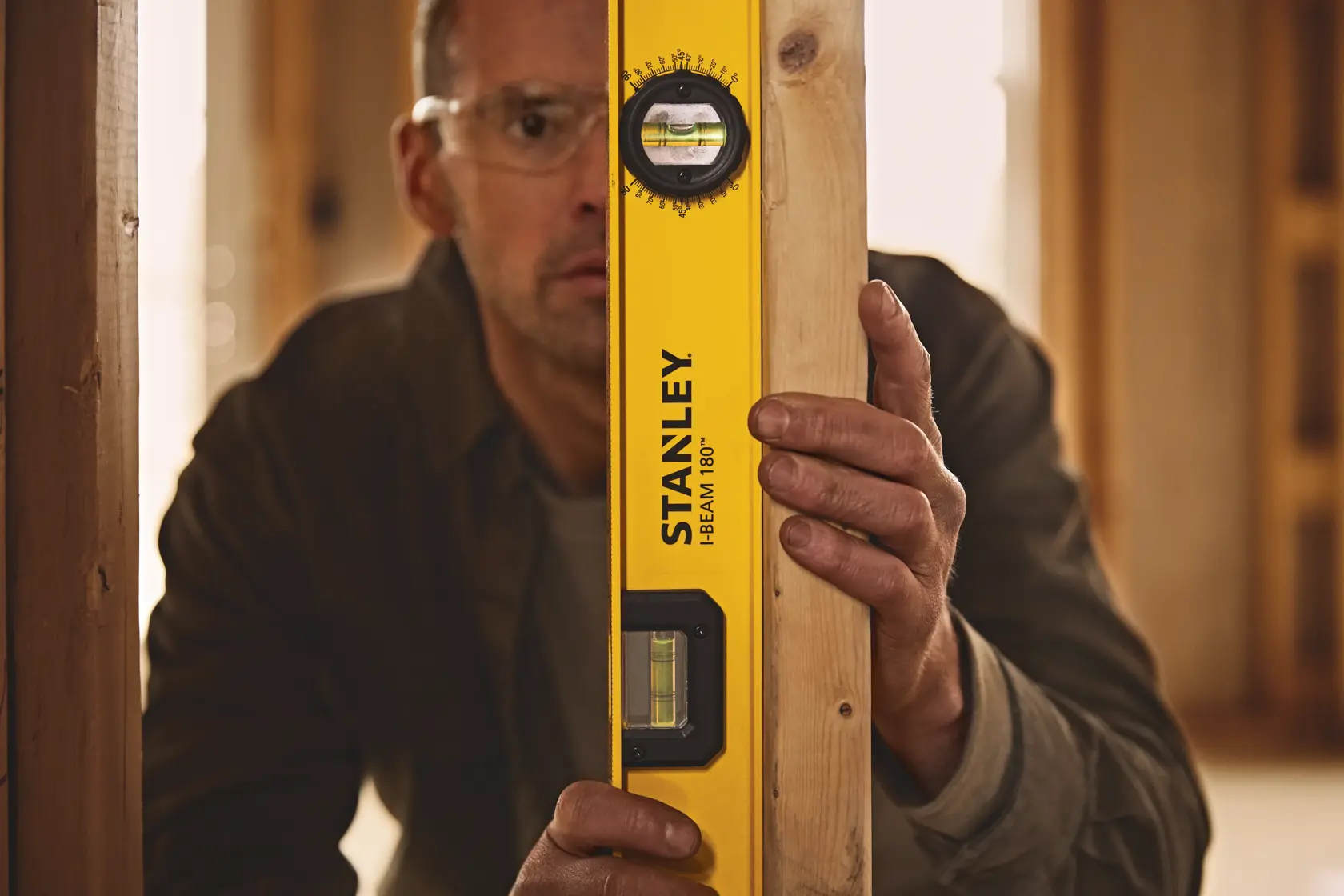 Photo of STANLEY 42-324 I-Beam 180° level tool being held against a wooden beam inside a construction site.