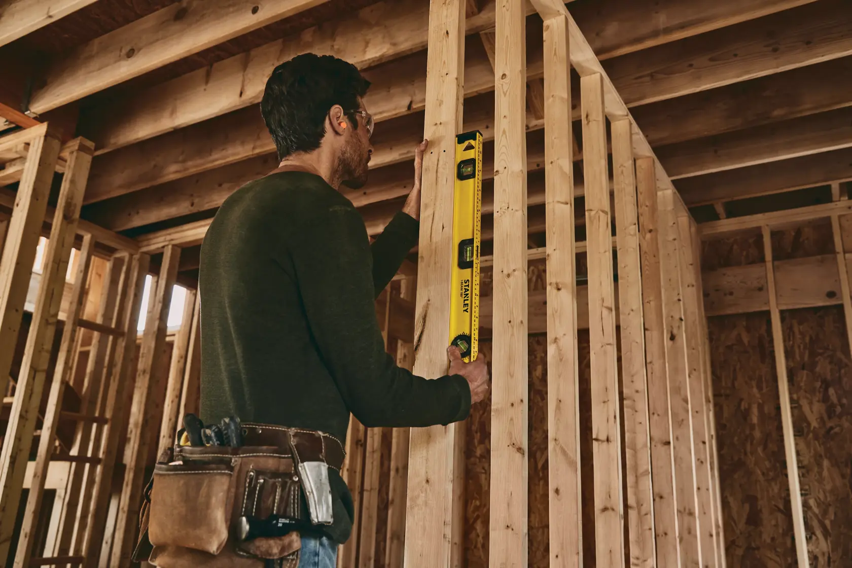 STANLEY 42-324 level tool used by worker checking vertical alignment of wooden studs at construction site.