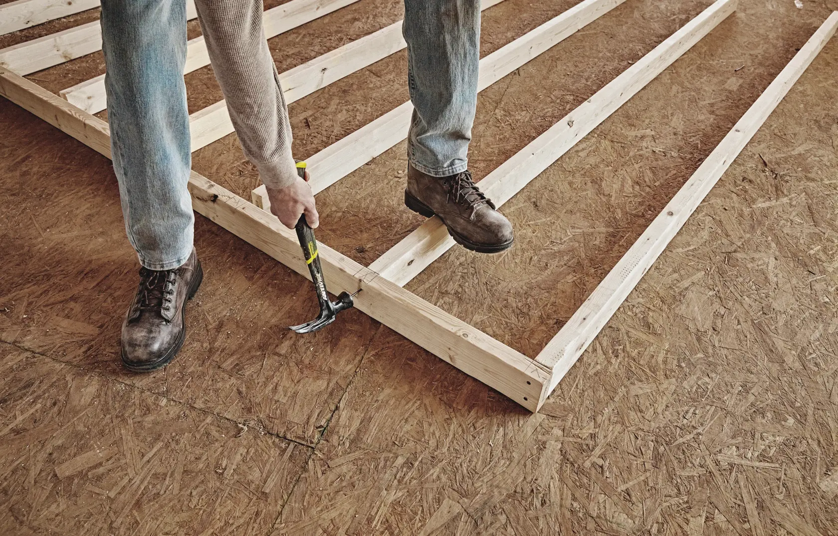 Photo of a person using a STANLEY 51-165 claw hammer to assemble a wooden frame on a plywood floor.