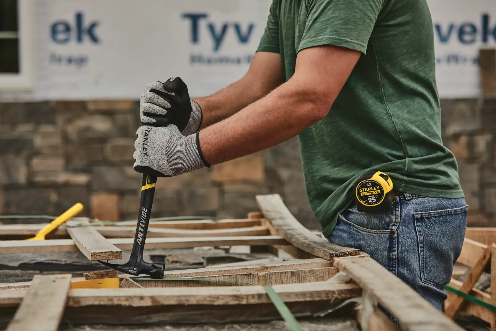 Photo of person using STANLEY 51-167 claw hammer on wooden boards at construction site, wearing gloves and jeans.