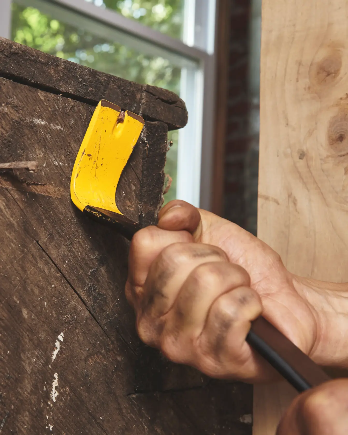 STANLEY 55-045 pry bar with yellow end being used to remove wood trim, close-up action shot.