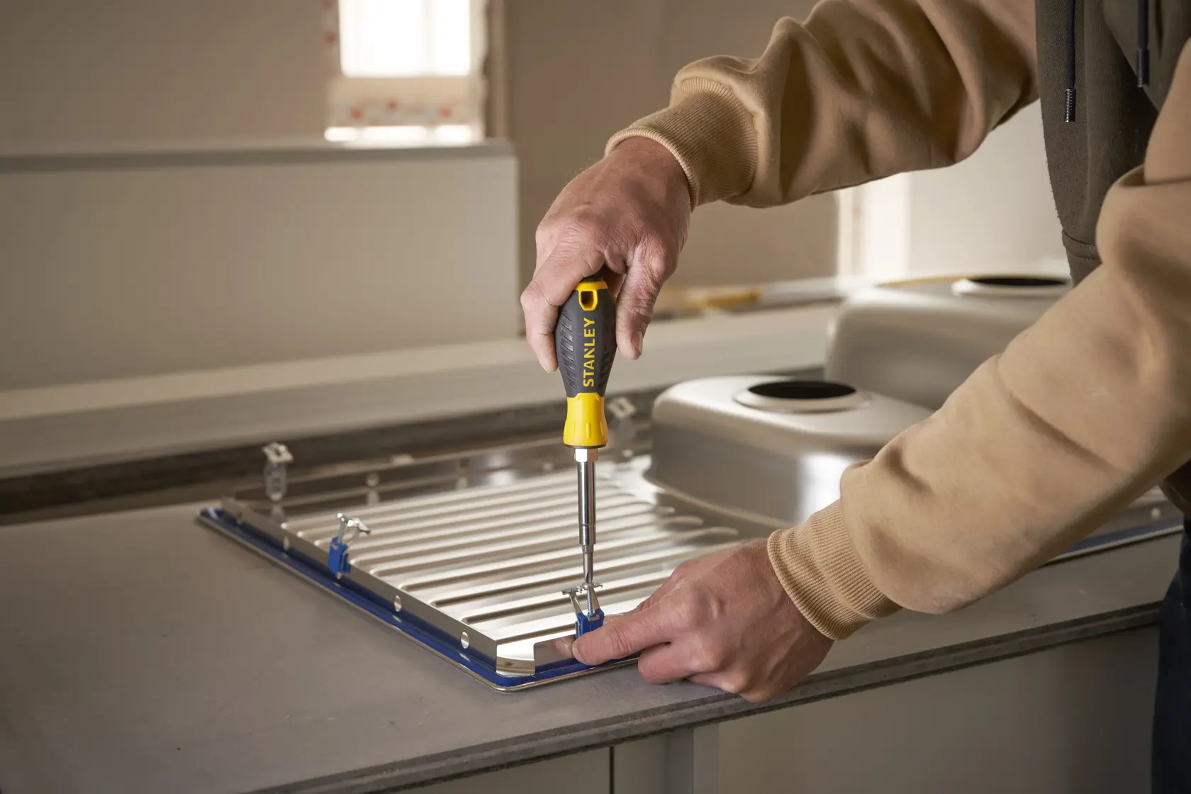 Photo of STANLEY 68-012 screwdriver in use, tightening a screw on a kitchen sink fixture installation.