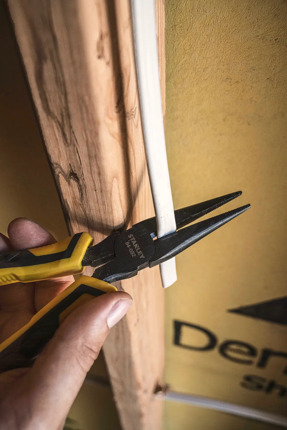Photo of STANLEY 84-032 long nose pliers holding a white wire against a wooden beam.