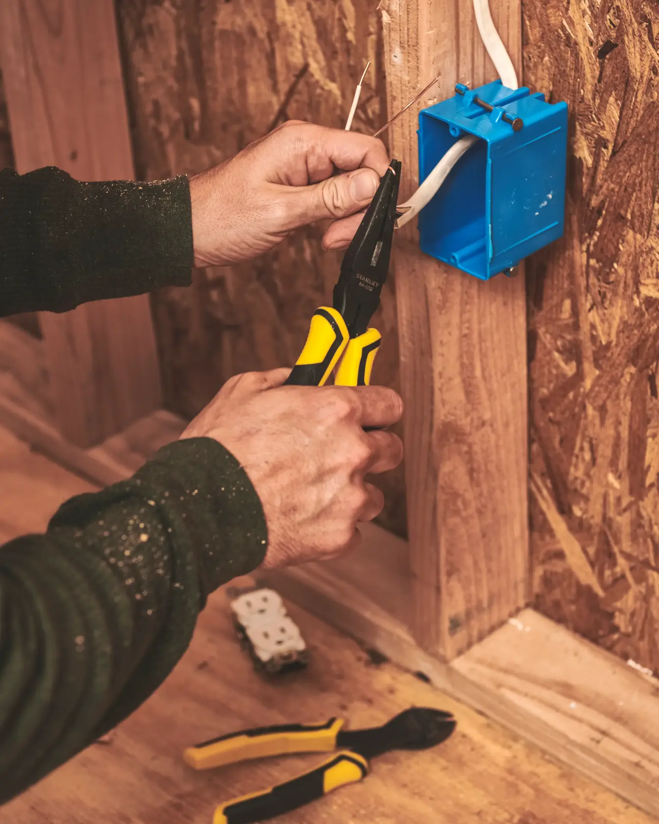 Stanley 84-032 pliers used for electrical wiring near blue outlet box, close-up angle.