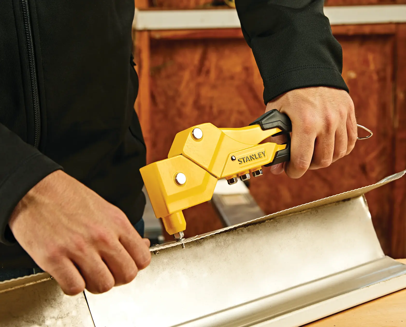 STANLEY MR77C rivet tool in use attaching metal sheets, close-up view.
