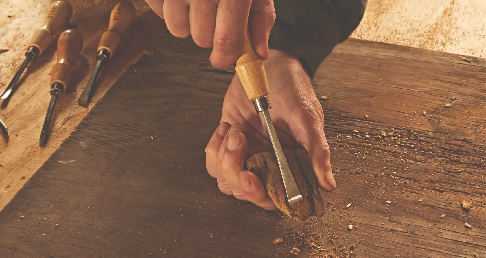 Photo of STANLEY STHT16863 wood chisel in hand carving wood, with other chisels on workbench.