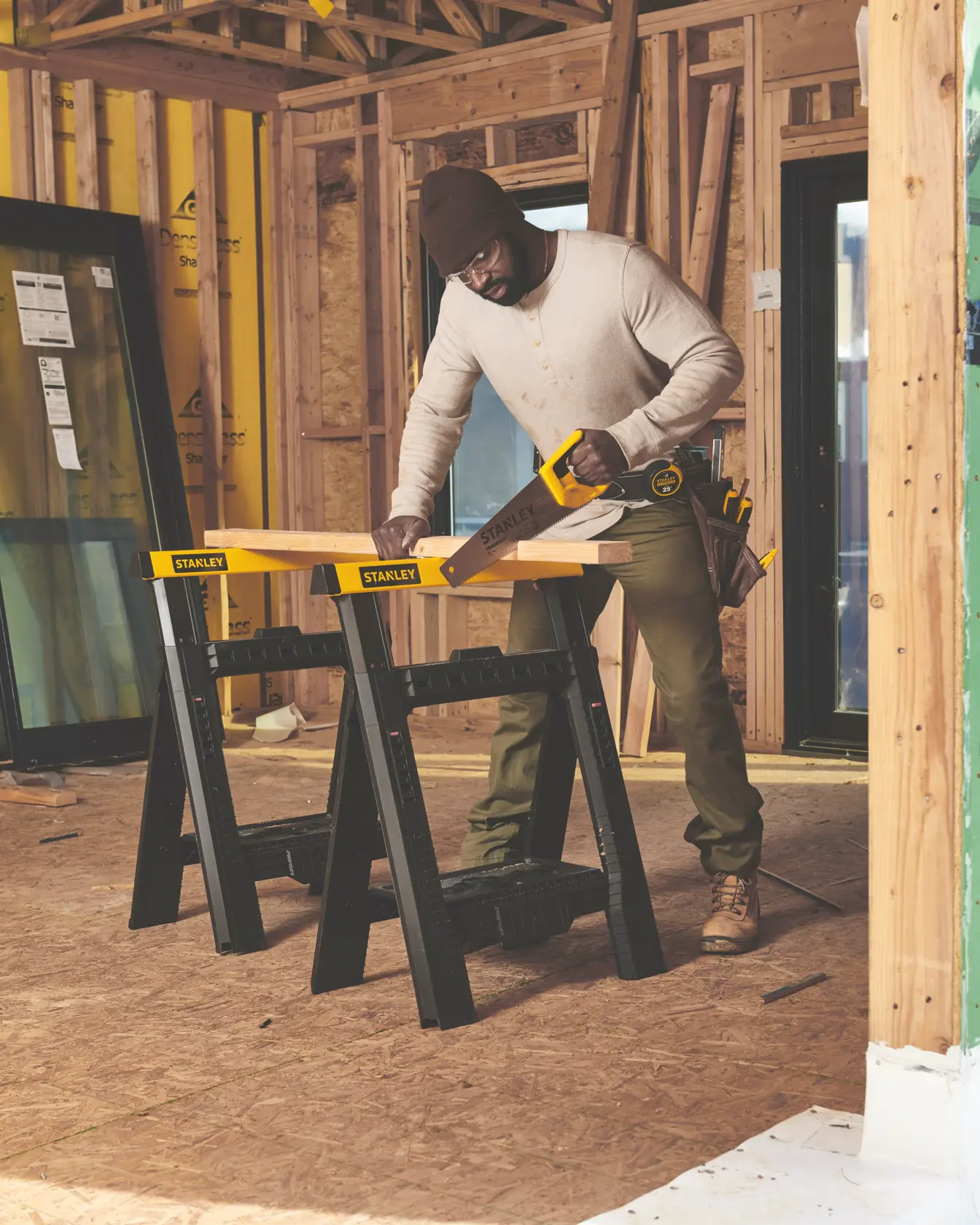 Photo of STANLEY STHT20348 handsaw in use on a construction site, cutting wood on black and yellow STANLEY sawhorses.
