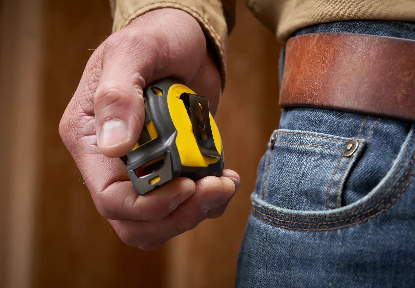 STANLEY STHT37242 tape measure with yellow and black casing held in hand next to jeans and brown leather belt.