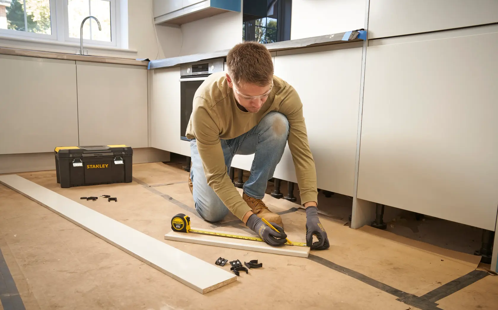 Photo of a person using a STANLEY STHT39525 tape measure in a kitchen renovation, STANLEY toolbox in background.
