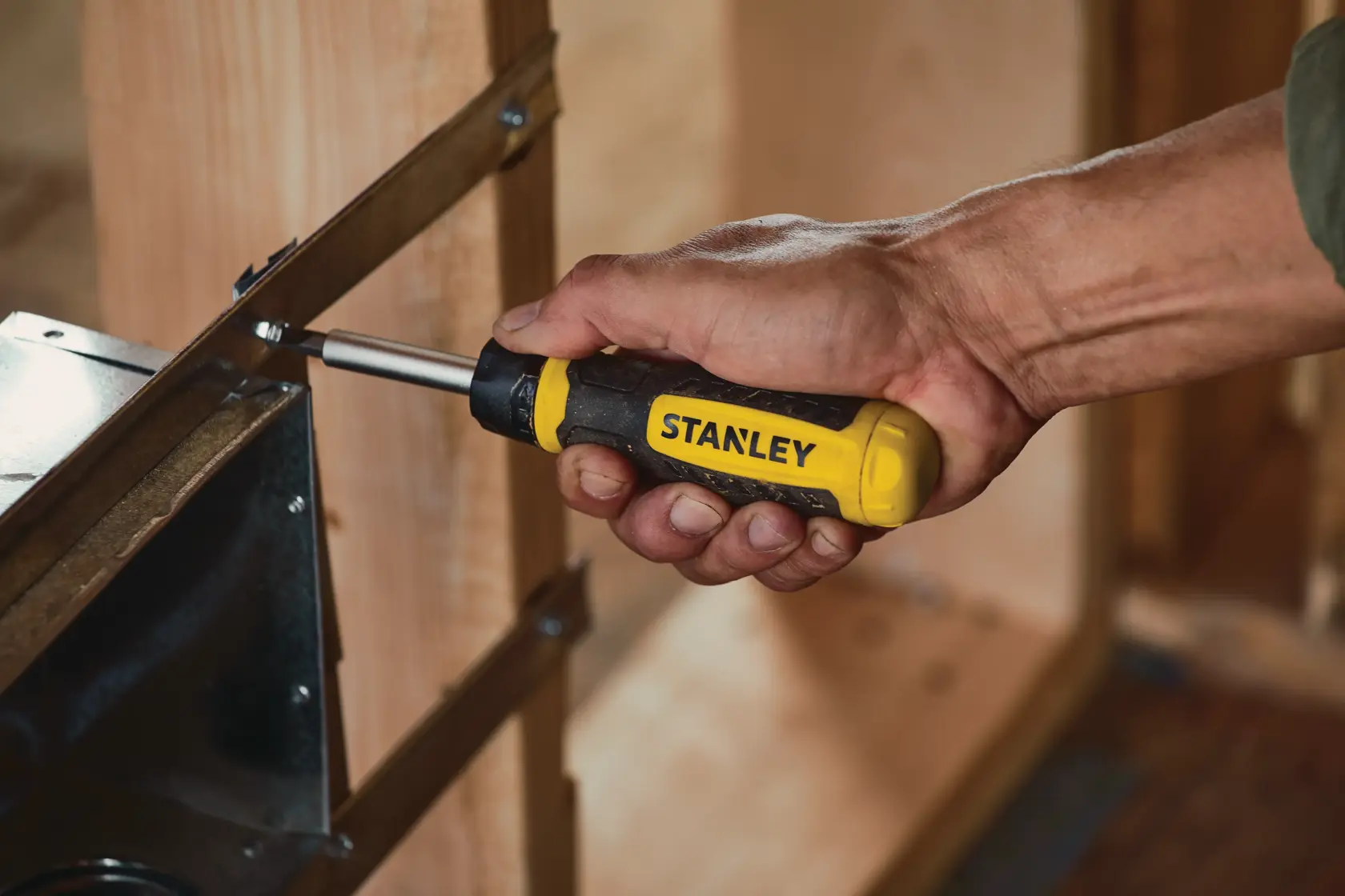 Stanley STHT60129 screwdriver being used to fasten a screw into a metal bracket on wooden framing.