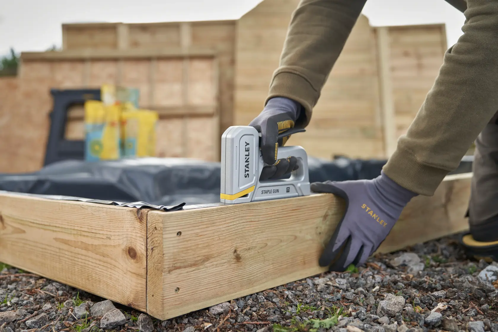 STANLEY STHT70150 staple gun in use fastening plastic to a wooden garden bed, angled side view.