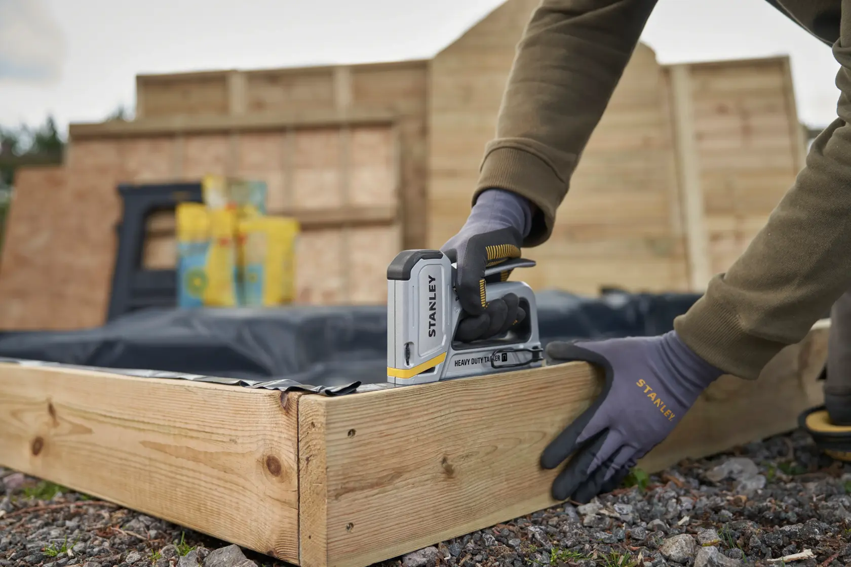 Photo of STANLEY STHT70250 heavy duty stapler being used to fasten material to a wooden frame outdoors.