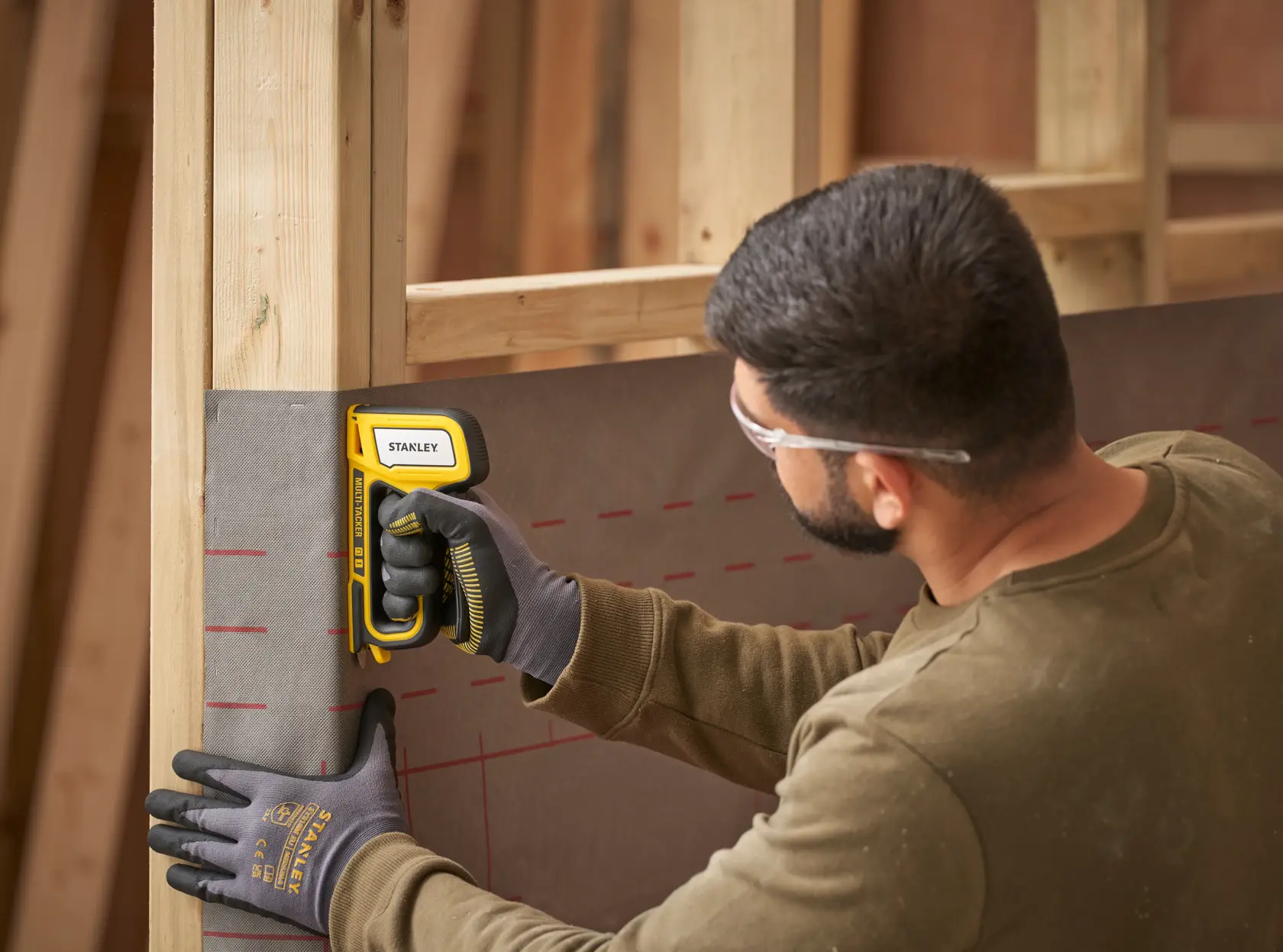 STANLEY STHT70440 stapler tool in use attaching material to wooden frame, close side angle.