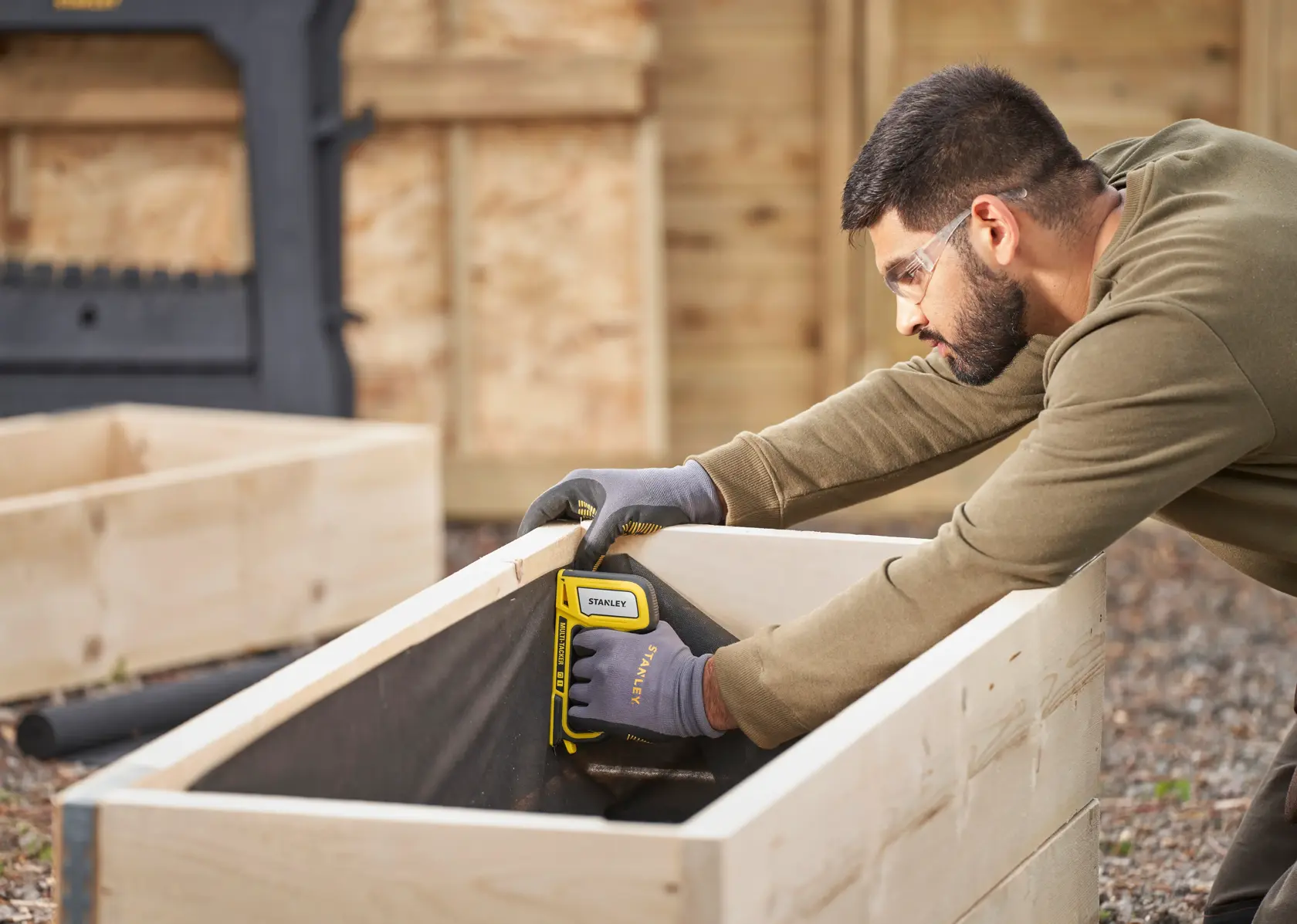 Photo of STANLEY STHT70440 staple gun used on wooden planter outdoors.