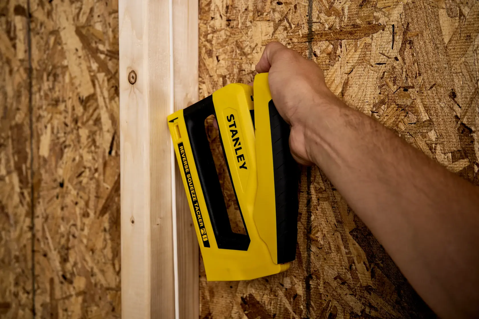 Photo of STANLEY STHT82551 stapler being used on wooden panel, yellow and black handheld tool.