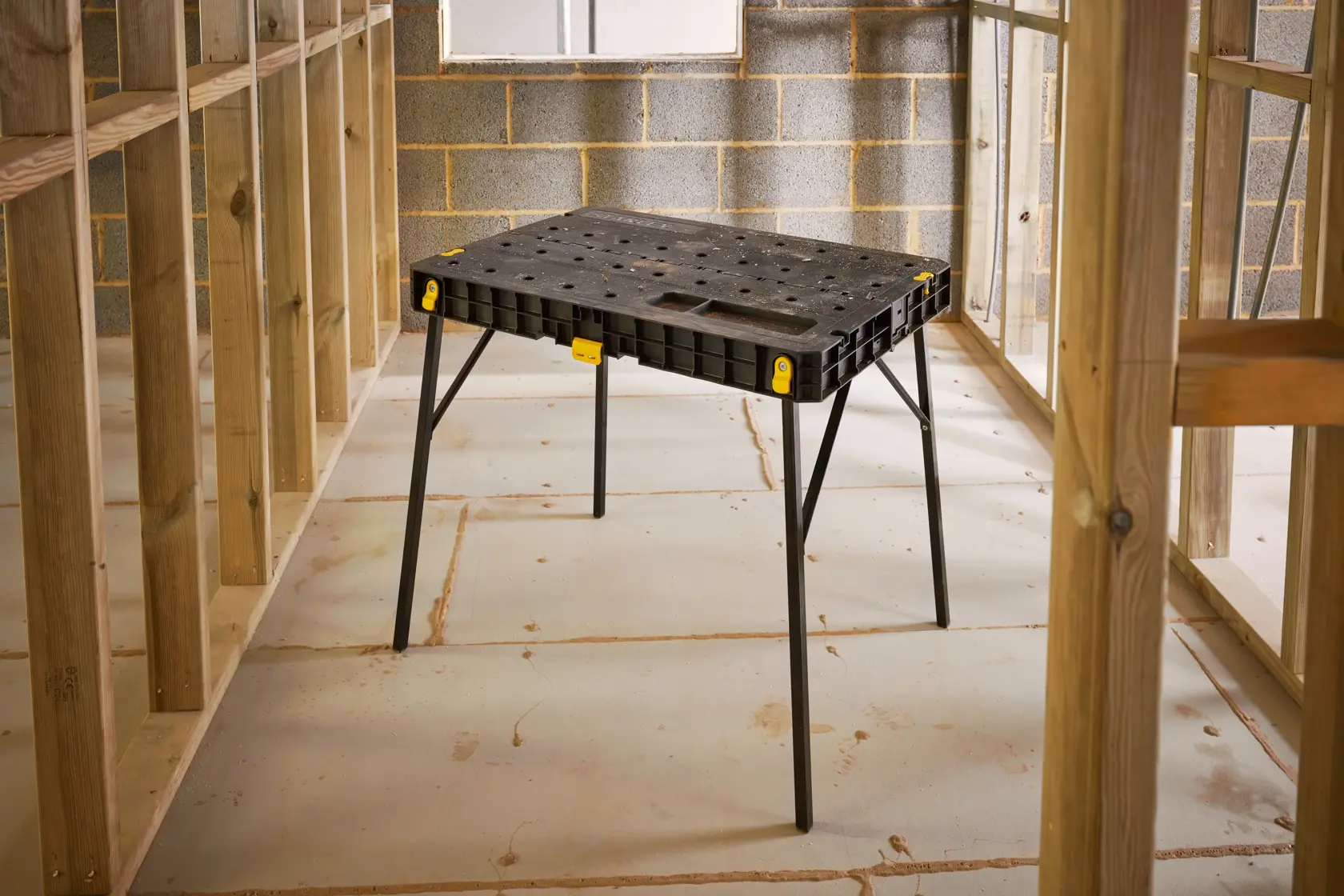 STANLEY STST11552 black plastic folding workbench with metal legs, shown at an angle in construction setting.
