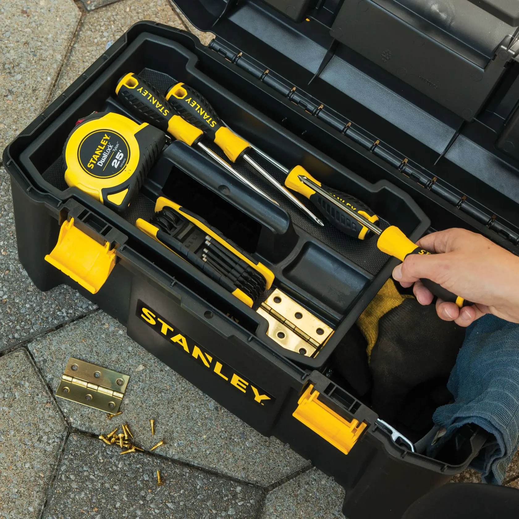 STANLEY STST19331 toolbox with yellow latch, screwdrivers, tape measure, utility knife, and hand holding a tool, top view.