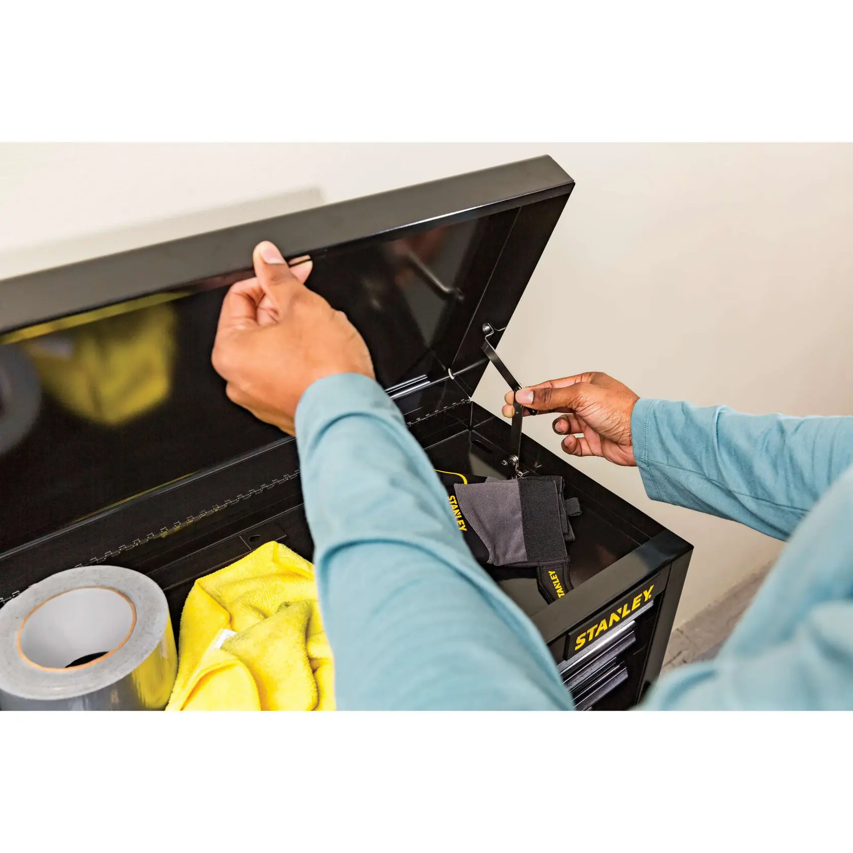Photo of a person opening a black STANLEY STST22656BK tool chest, showing interior storage with tape and cloth.