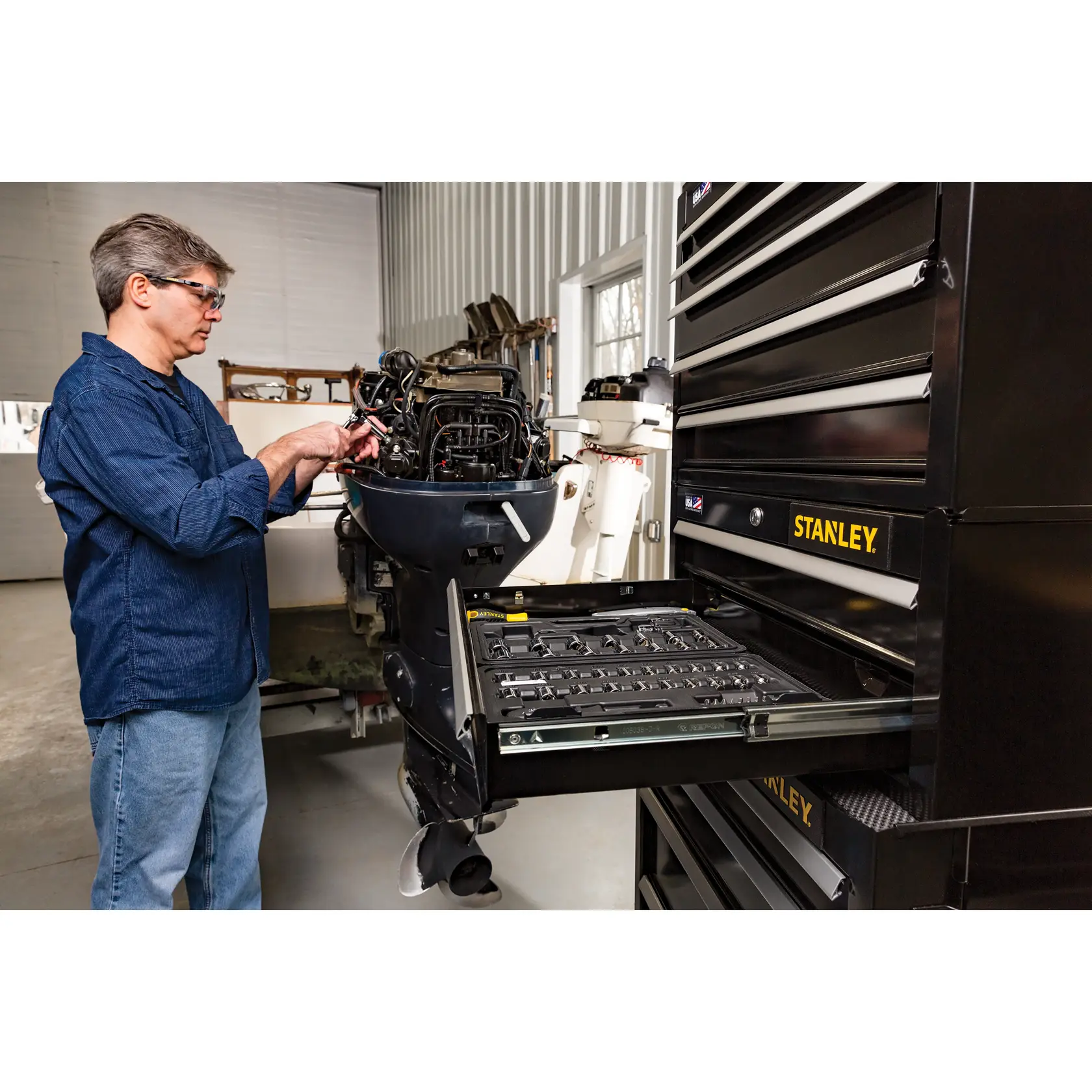 Photo of a STANLEY STST22657BK black tool chest with open drawer, showing organized hand tools in a workshop.