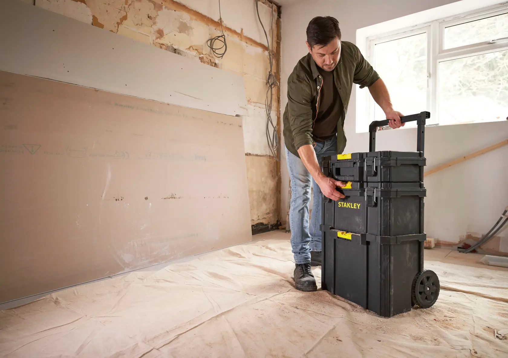 Photo of STANLEY STST60500 rolling tool storage box with yellow latches in a construction room, person adjusting handle.