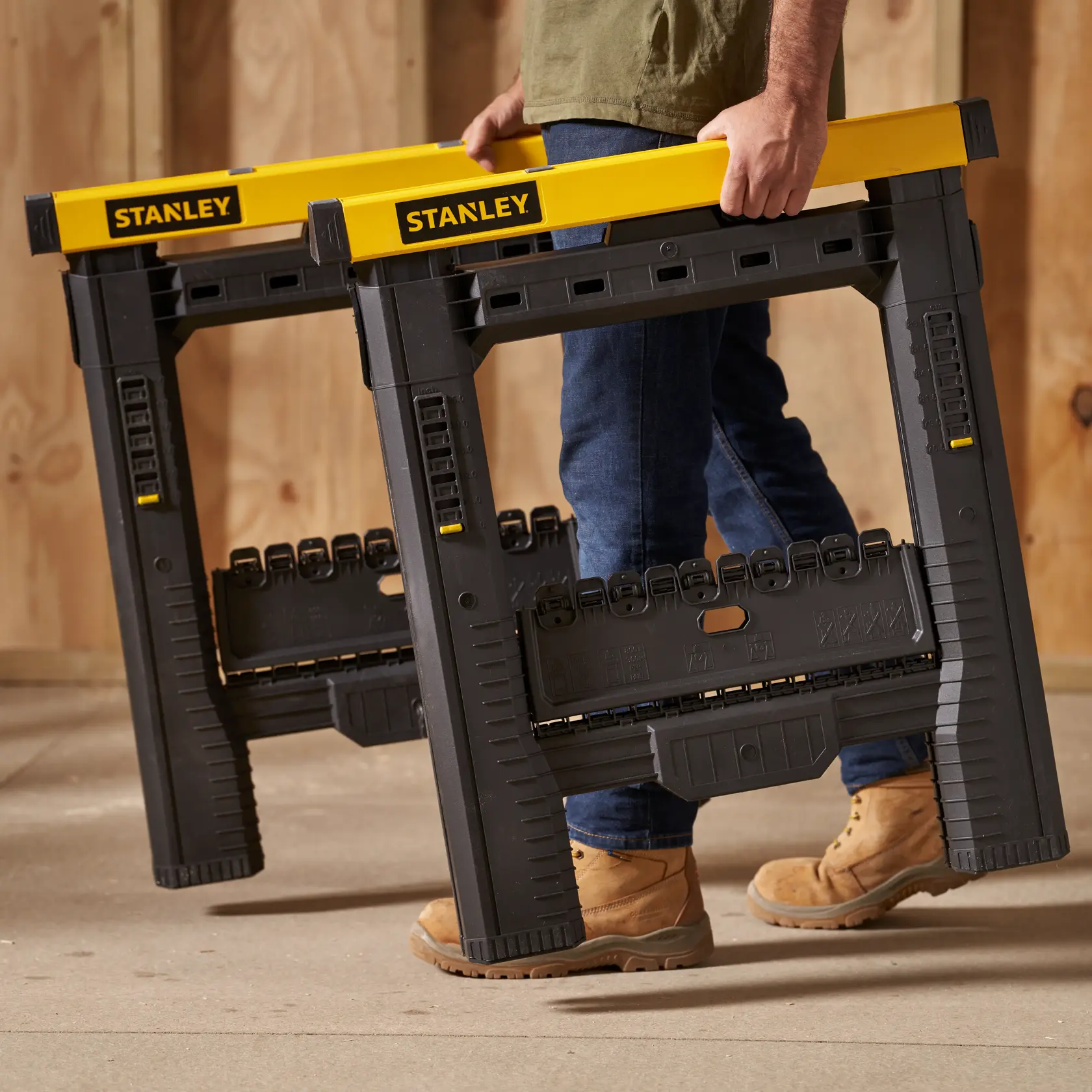 STANLEY STST60626 black and yellow portable sawhorses carried by person in workshop setting.