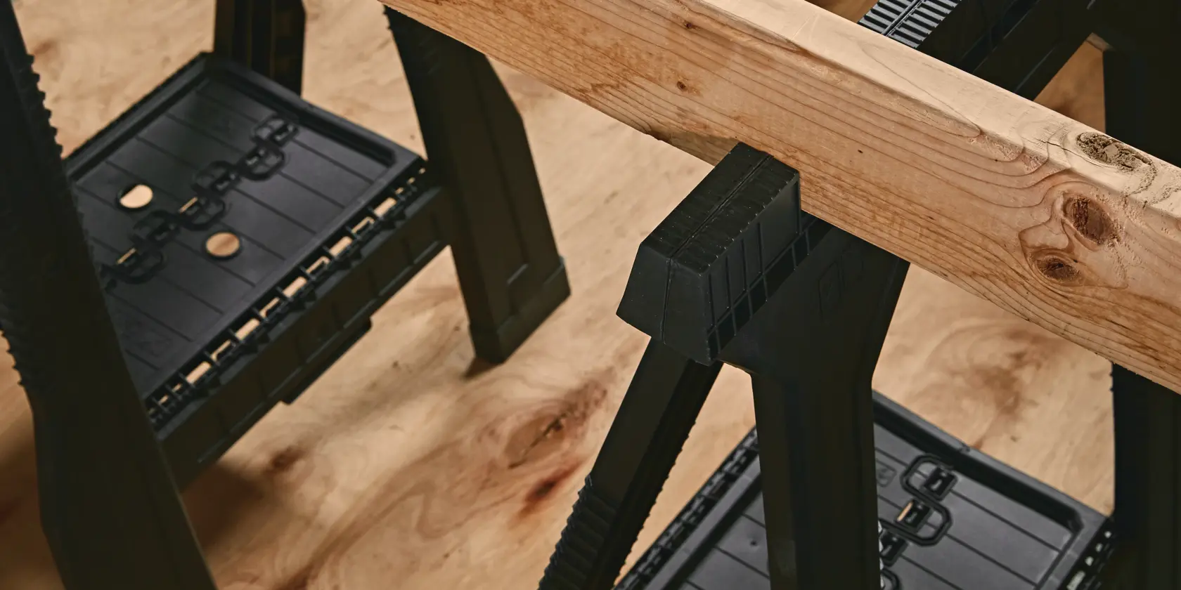 STANLEY STST60952 black plastic sawhorses supporting a wooden beam, top view on wood floor.